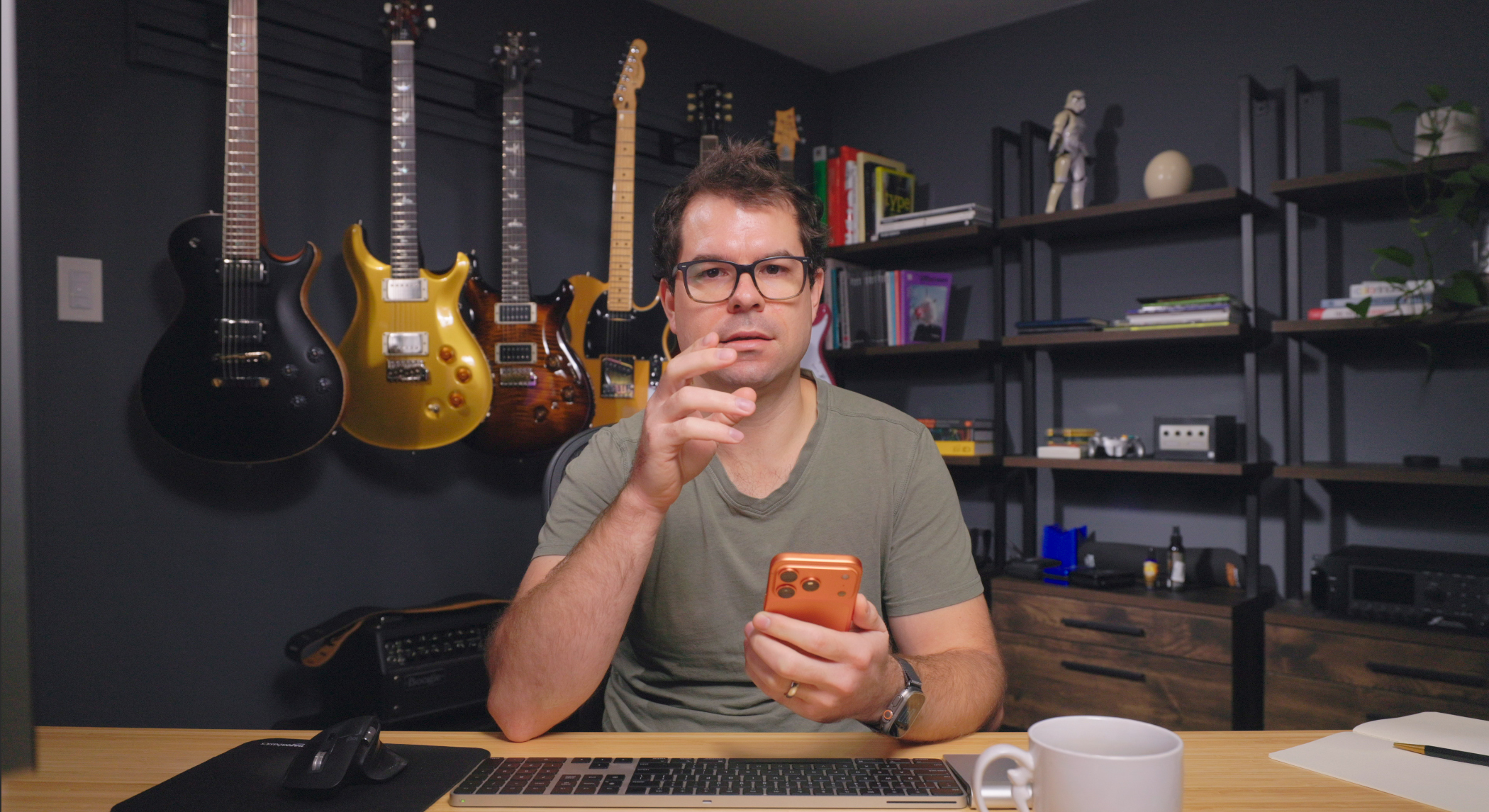 An image of Nathan at his desk. The camera is sitting where the monitor would normally be, and facing him dead on. Nathan is holding an iPhone in one hand and gesticulating with the other.